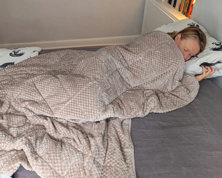 The writer lays on a bed wrapped in the OHS Waffle weighted blanket