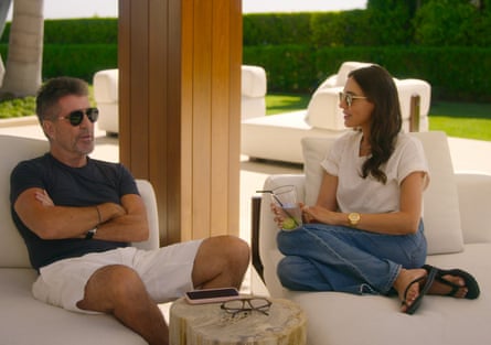 Simon Cowell and Lauren Silverman sitting on outdoor sofas wearing sunglasses