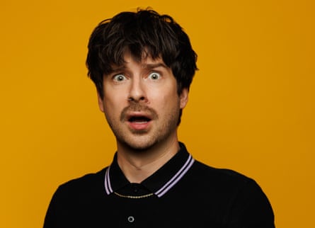Stott looking startled, in black shirt with banded white collar.