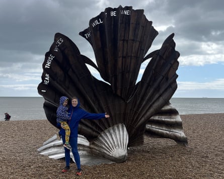 Woman holds child and gestures in front of sculpture