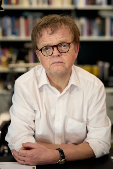 Jones as Rusdridger, wearing glasses, in front of a blurred bookcase