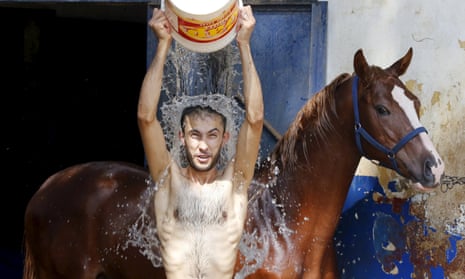 A man pours water over himself while washing a horse to try to cool both of them down in Beirut.