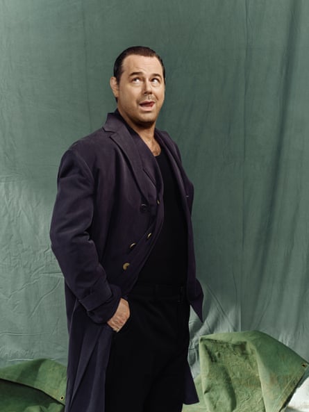 Danny Dyer wearing all black outfit against a green background and looking upwards