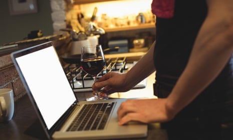 A man standing at a kitchen worktop with a laptop and a glass of red wine