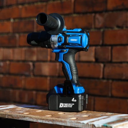 Draper D20 20V Brushless Combi Drill stands upright on a wooden work bench in the sunshine against a red brick wall.