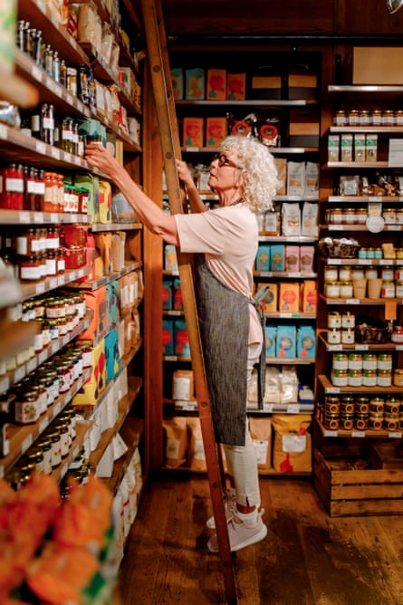 Side view of senior female owner standing on ladder and doing inventory at supermarketGettyImages-2170048160