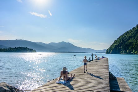 A view of bathers on a jetty into a blue lake, with hills in the distance