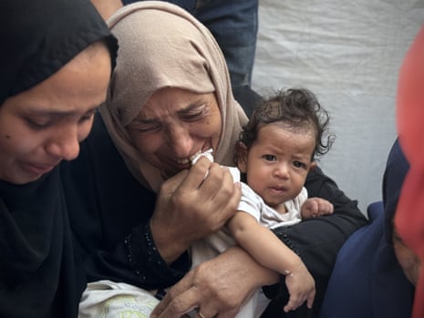 A woman holds a baby while crying after an Israeli army attack on the Morag area in the northern part of Rafah, Gaza Strip.