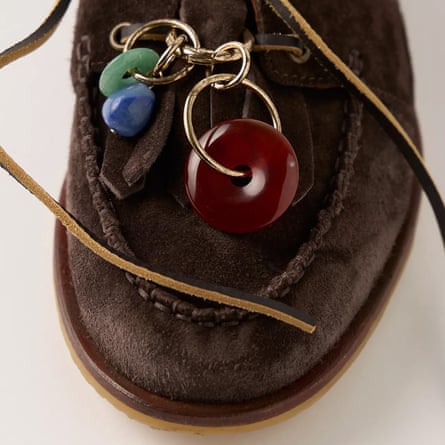 A close up of a dark brown loafer with stone charms on the bottom lace