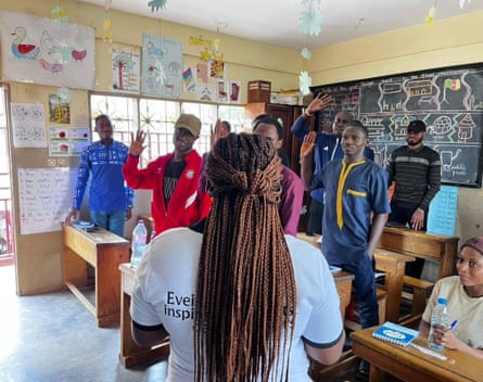 A woman with long braids has her back to the camera addressing a group of men in a classroom.