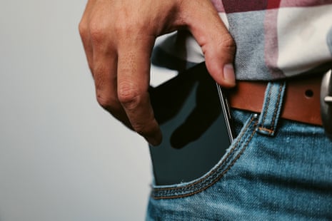 Male hand sliding mobile phone either into or out of denim jeans pocket