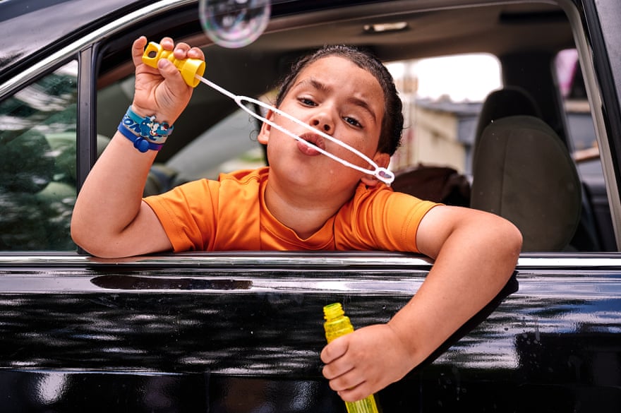 Boy in orange shirt blows on a bubble stick inside a car