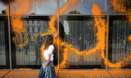 A protester smears orange paint over the glass facade of a building