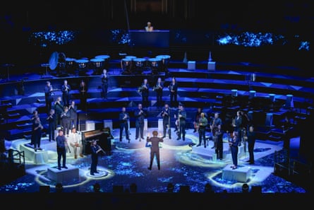 A conductor during a performance in front of an orchestra, with blue stage lighting.