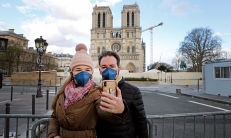Tourists wearing protective masks take a selfie in front of Notre Dame cathedral