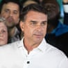 Flavio Bolsonaro speaks before microphones at a press conference, surrounded by onlookers