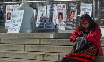 woman in red sits on steps in front of signs with faces and names of missing women