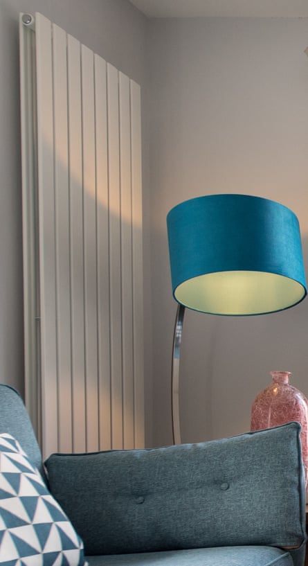 A retro looking blue sofa, a floor lamp and modern upright radiator within a home