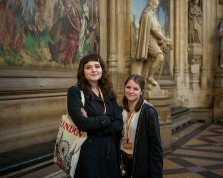 Two young women stand next to a statue in the Houses of Parliament, London.