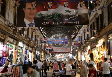 People shop at the Al-Hamidiyah Souq, decorated with banners depicting Syria's president Bashar al-Assad.