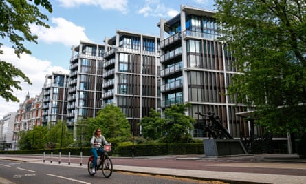 A row of four modern low-rise luxury blocks of flats on a tree-lined road, with a woman cycling past