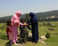 One woman holds a child by the chin as another administers drops into their mouth in a green rural setting. Two other children stand next to them