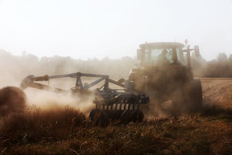 A farmer crops the land on a tractor, with dust flying in the air.