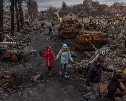 A person in a red coat and another in a pale blue coat walk past damaged machinery
