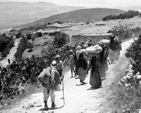 Black and white photo of people walking on a road carrying their belongings