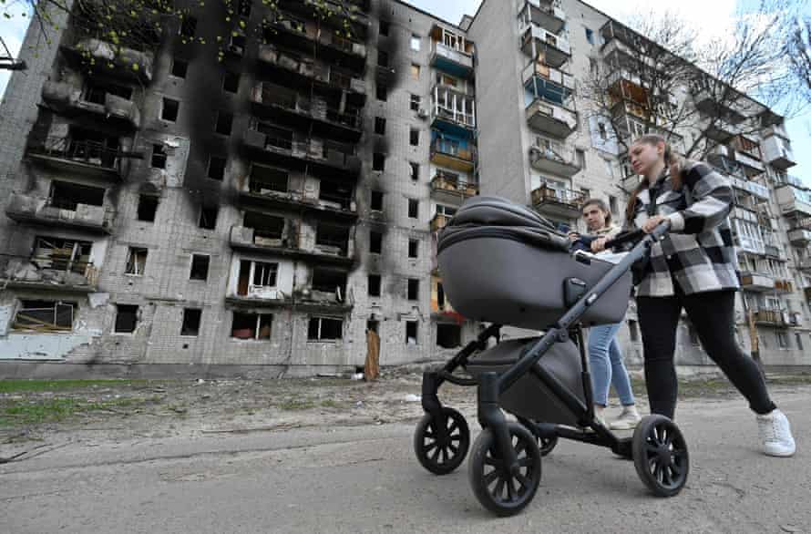 A woman pushes a pram past a heavily damaged residential building in Chernihiv.