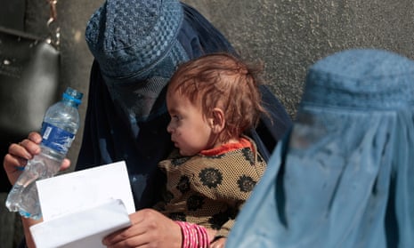 A displaced Afghan woman holds her child as she waits with other women to receive aid supply outside an UNCHR distribution centre on the outskirts of Kabul.