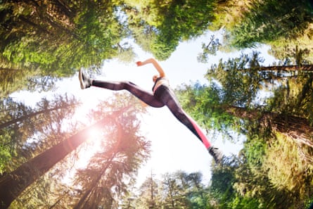 A woman leaping in a sunny forest, seen from below