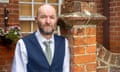 Christopher Marsh, 49, at his home in Ramsgate. He is standing in front of a red-brick house with a hanging basket of flowers behind him and a tall brick gatepost to one side. He has a short, tidy greying beard and a bald head, and is dressed smartly in a white shirt, pale green tie and navy blue waistcoat. He is looking straight at the camera without smiling and his eyes are narrowed as if he is facing the sun.