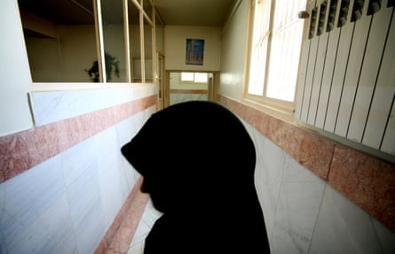 A woman wearing a head covering is seen in profile in a narrow corridor.