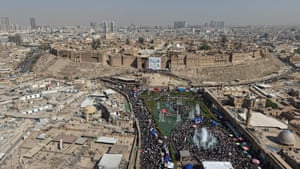 An aerial shot of a crowd of people in a park making their way up to a citadel behind them
