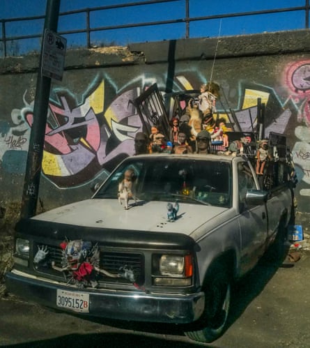 Pickup truck with toys stuck on to it in front of a graffiti-covered wall.