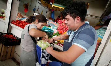 A vendor helps a woman to arrange items in a bag at a market.