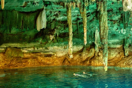 Very beautiful scene with blue water, sandstone coloured banks and turquoise stalactites descending. Two swimmers on their backs in the water
