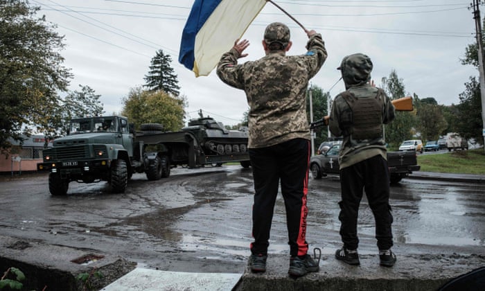 Two boys cheer to passing vehicles from their mimicked checkpoint at the curve of a road in Chuhuiv, Kharkiv region.