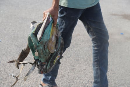 A an’s hand holds a tattered and dust covered child’s backpack.