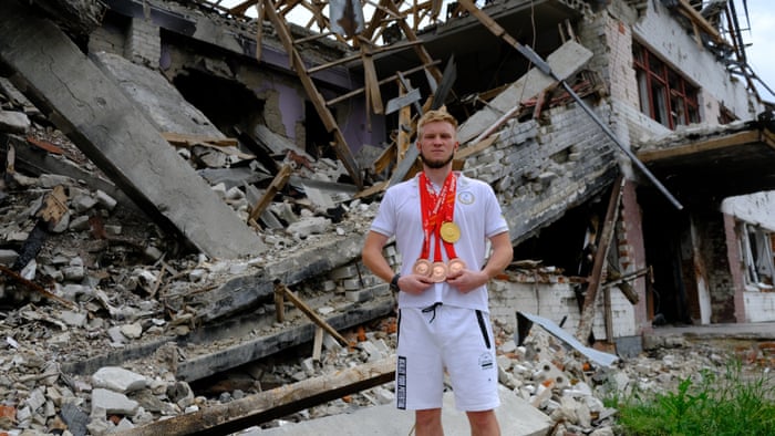 Ukrainian Paralympic athlete Dmytro Suiarko poses for a photo on 4 July with his medals in front of the debris of his once training school in Chernihiv. Suyarko has auctioned a bronze medal for $5,300 to donate to the Ukrainian army.
