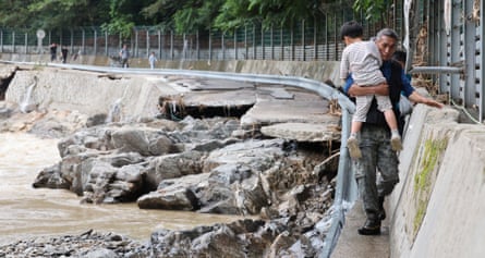 A man carries a child to safety along a narrow ledge next to where a road has collapsed into a river