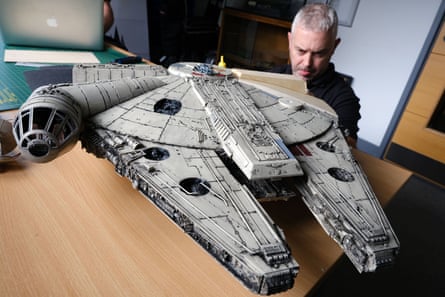 A man stands by a model of the Millennium Falcon spaceship which is on a wooden tabletop.