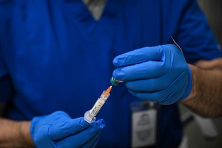 person in blue scrubs and gloves prepares to administer a vaccine