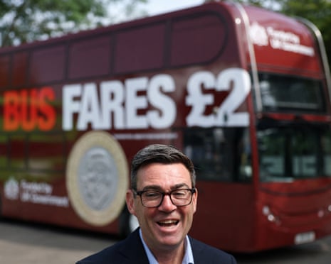 Andy Burnham smiles broadly in front of a red double-decker bus displaying bus fares