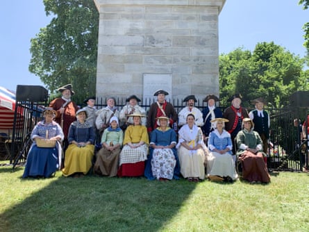 men and women in Revolutionary War era attire sit and stand for a group photograph