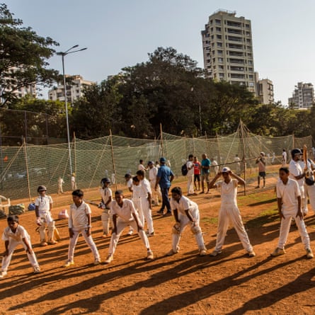On the cricket pitch named New Hind at the Gymkhana Matunga, children in a semi-circle practise catching balls hit by a coach. Coaches rent out pitches by the hour and give paid lessons to players of all ages.