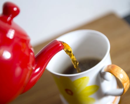 Tea is poured from a red teapot into a mug with a yellow flower motif