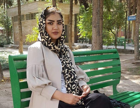 A young woman in a headscarf sits on a park bench