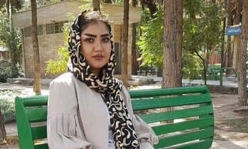 A young woman in a headscarf sits on a park bench